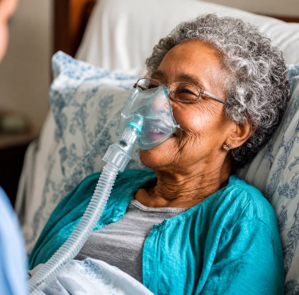 Senior woman resting in bed using an oxygen mask, receiving supportive home health care in Bedford, Indiana.