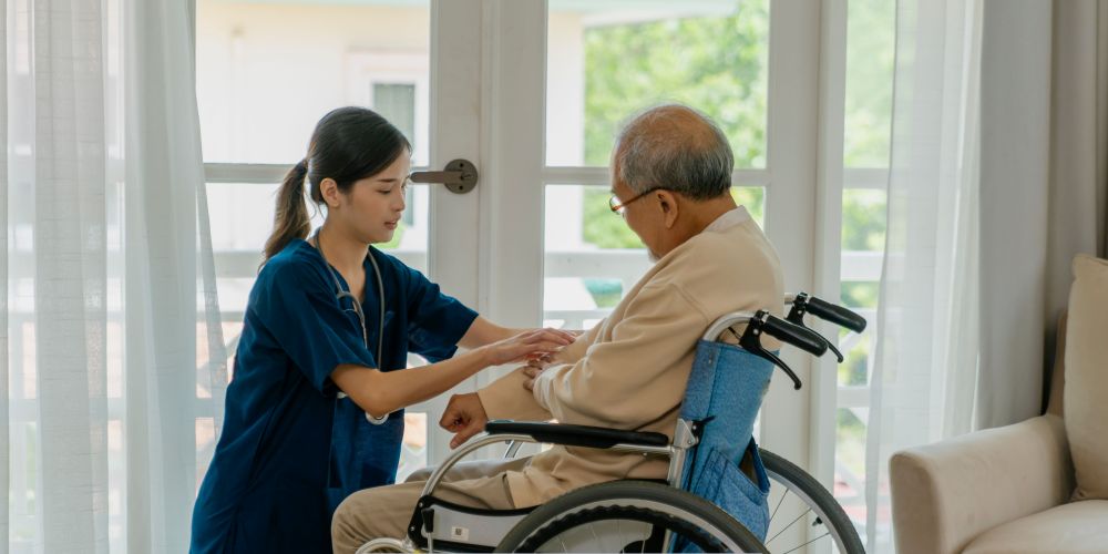 Home health care in Greenfield, IN caregiver assisting an elderly man sitting in a wheelchair at home during a supportive visit.