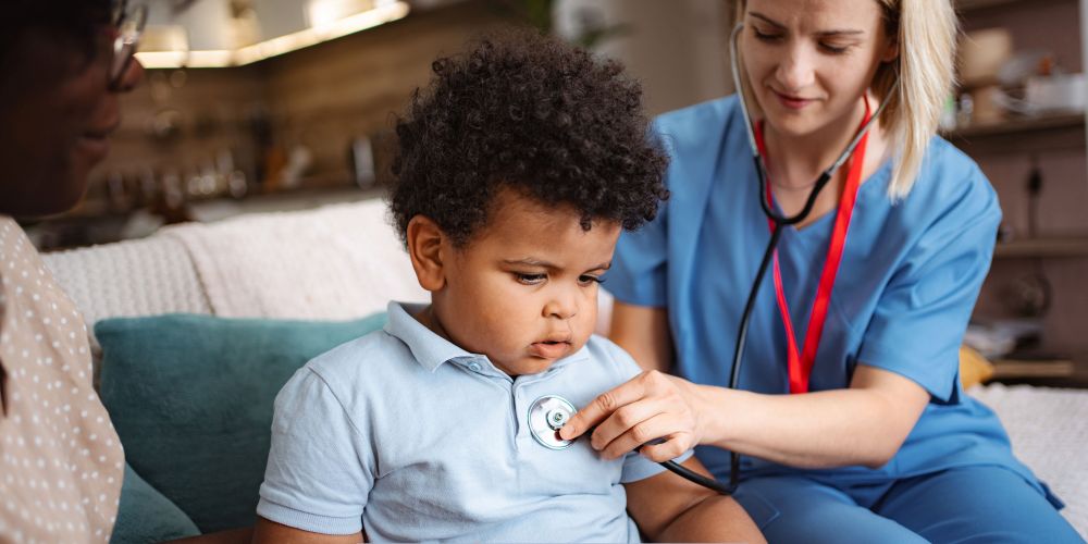 Home health care in Greenfield, IN nurse using a stethoscope to check a young child while the parent sits nearby at home.